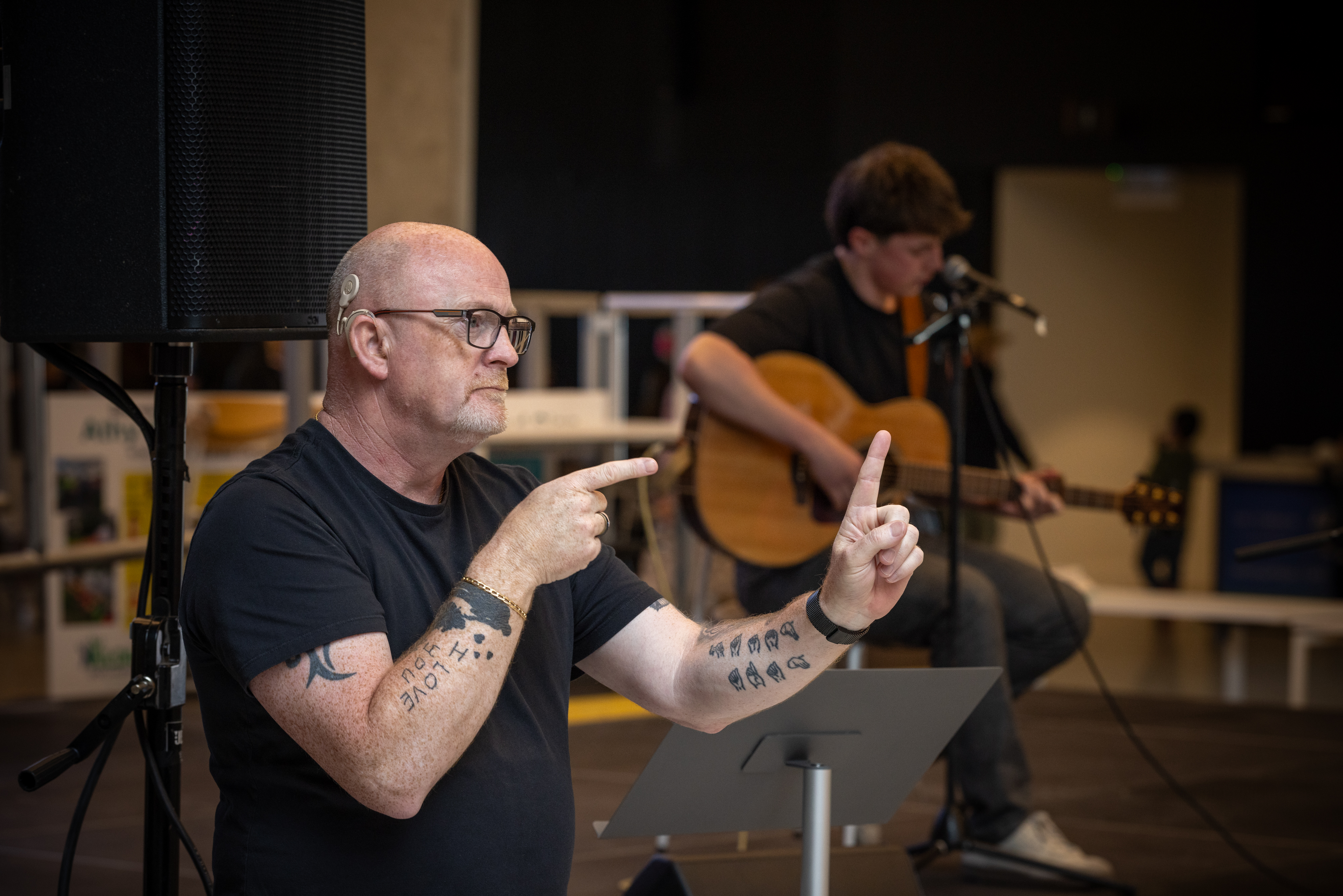 A person singing on stage with playing guitar , accompanied by a sign language interpreter. 